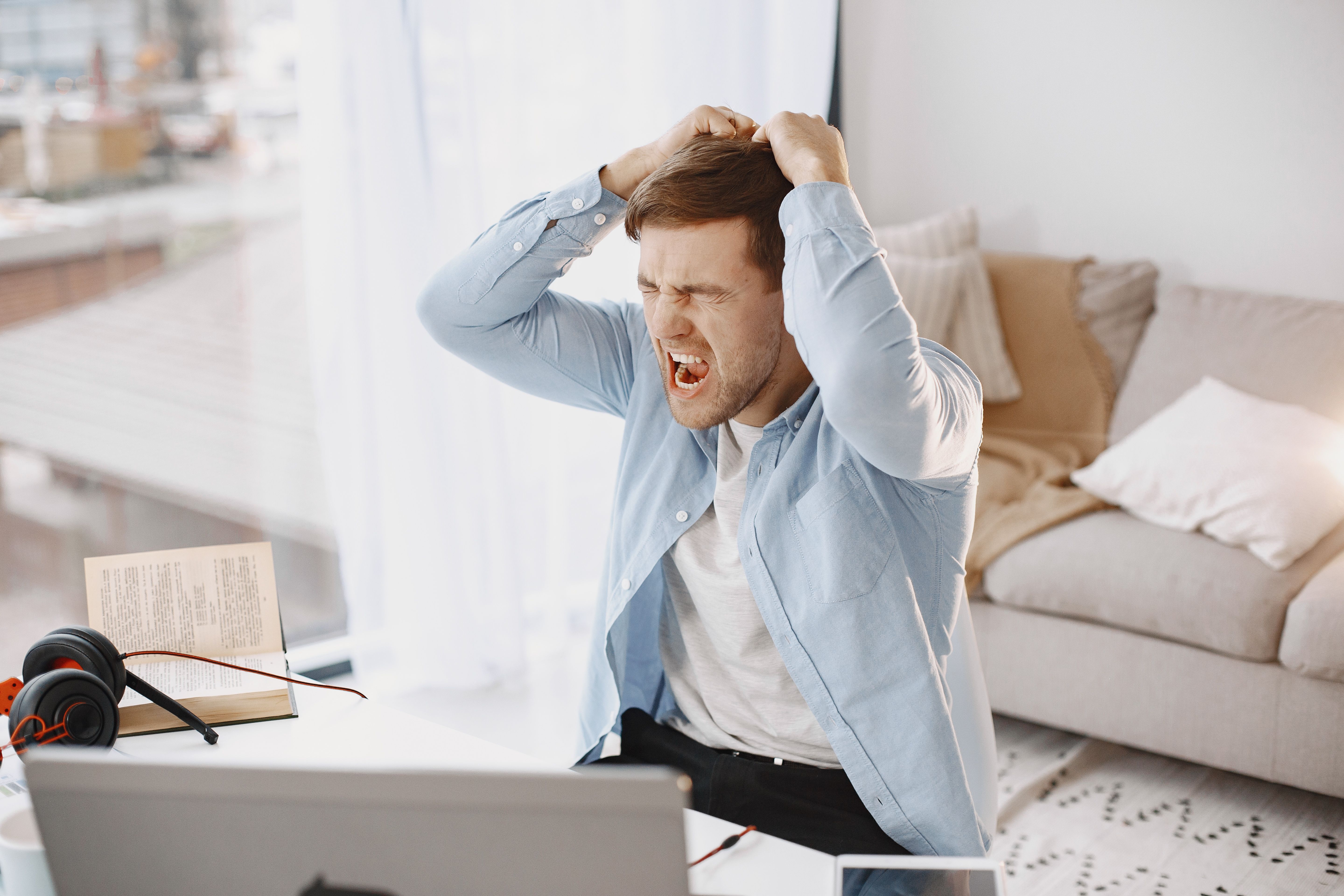 An upset man with his mouth open, pulling his hair at a desk with a laptop in a home setting. (Representative Cover Image Source: Pexels | Photo by Gustavo Fring)
