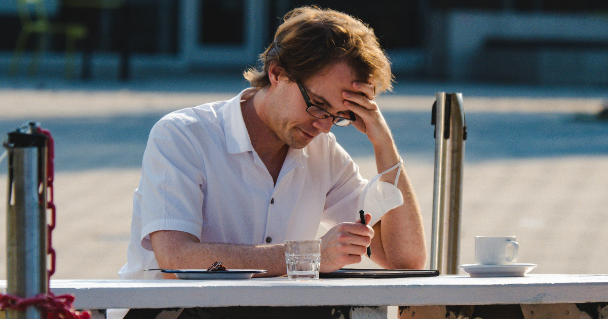 Man sitting outside with a laptop, looking dissapointed.