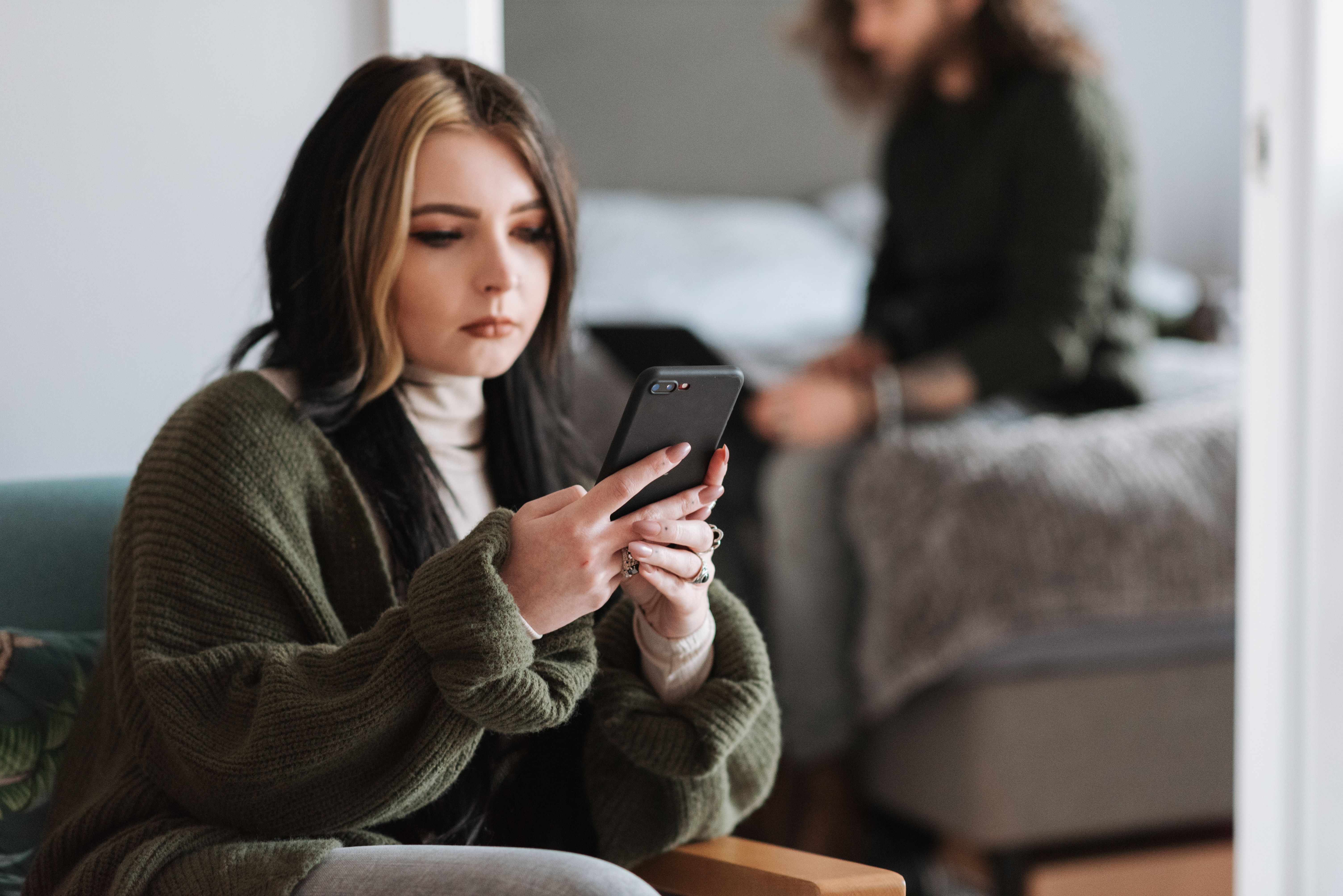 A woman is checking phone while boyfriend is sitting on the bed. (Representative Image Source: Pexels | Photo by Anete Lusina)