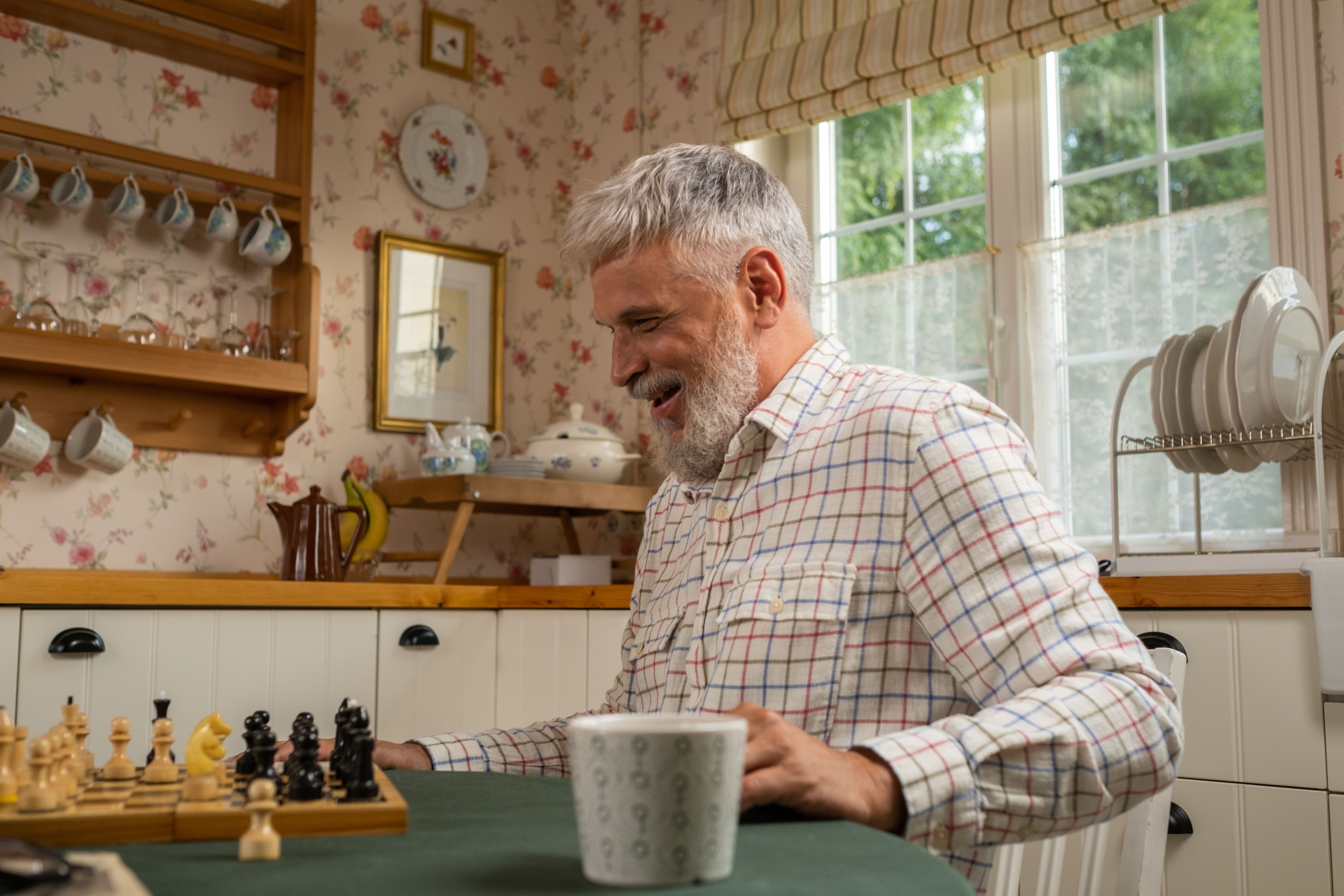 Smiling elderly man in a plaid shirt playing chess. (Representative Cover Image Source: Pexels | Photo by Ron Lach)