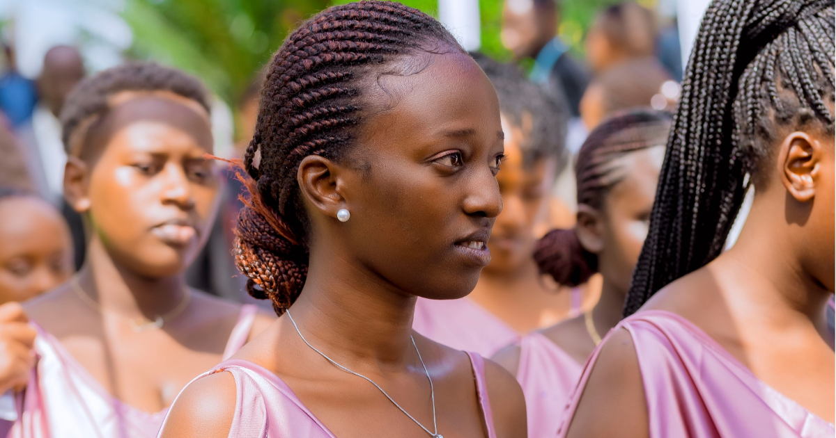 Group of bridesmaids in pink dresses with braided hairstyles at an outdoor event, looking confused.
