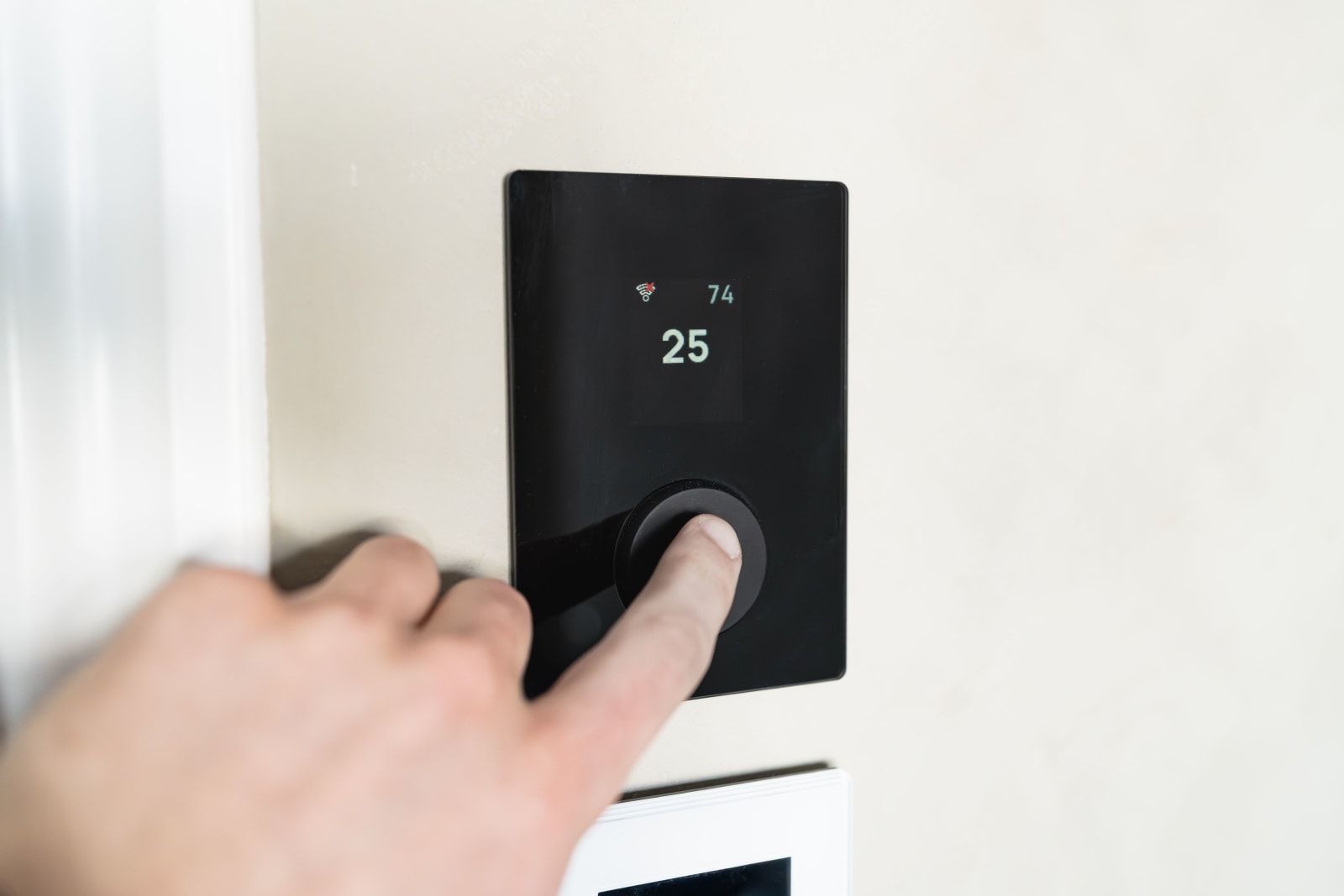 Close-up of a hand adjusting a sleek, modern smart thermostat on a wall