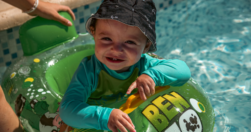 Adorable toddler in sun hat and green swim ring smiles while enjoying a sunny pool day (Representative Image Source: Pexels | Photo by Franco Monsalvo)