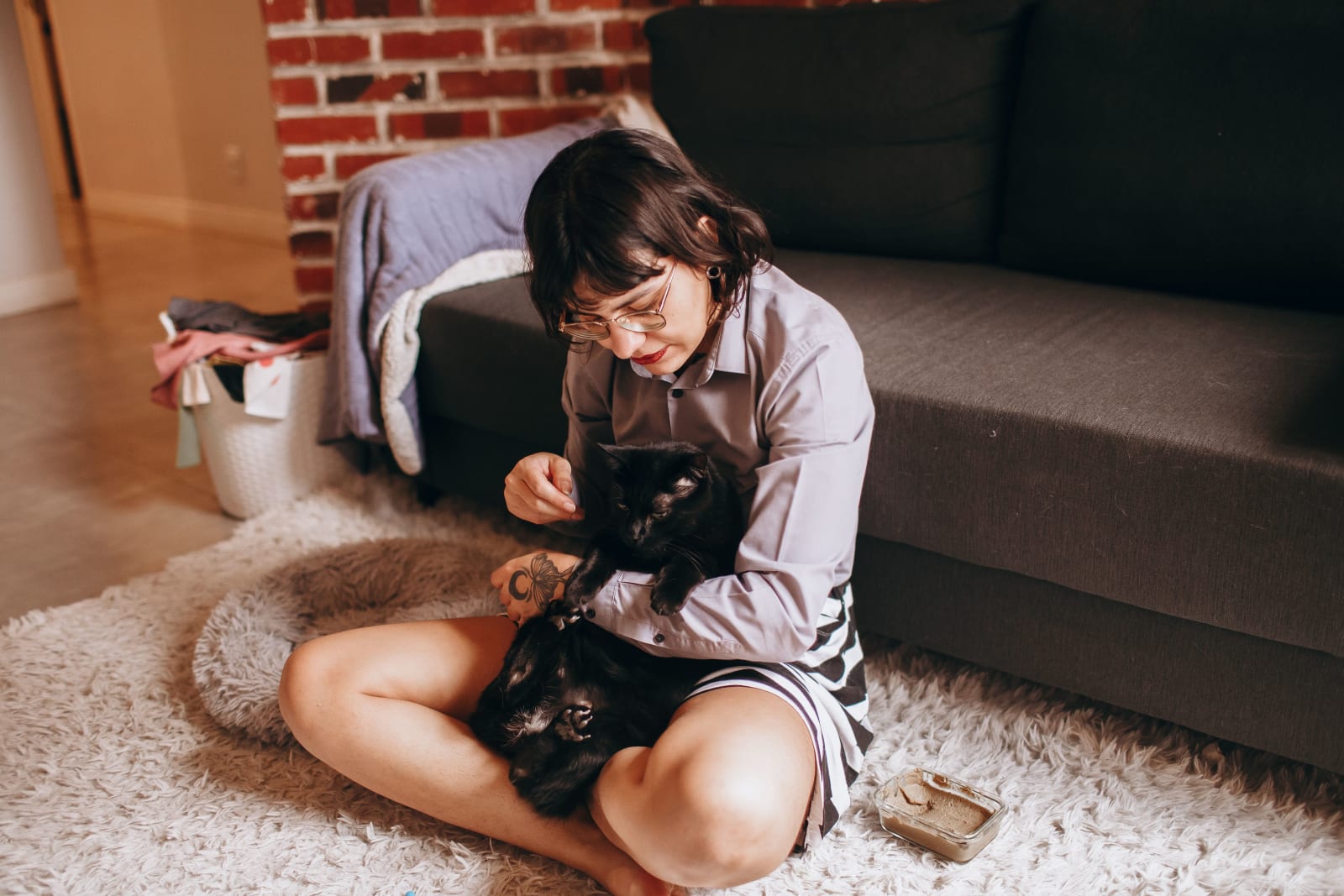 A woman lovingly pets her two black cats while sitting on a soft rug in a cozy living room