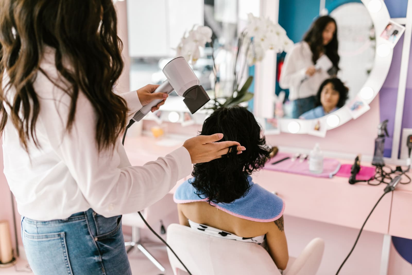 A hairstylist uses a hairdryer on a client at a modern salon with a mirror reflection. (Rperesentative Image Source: Pexels | Photo by RDNE Stock project)