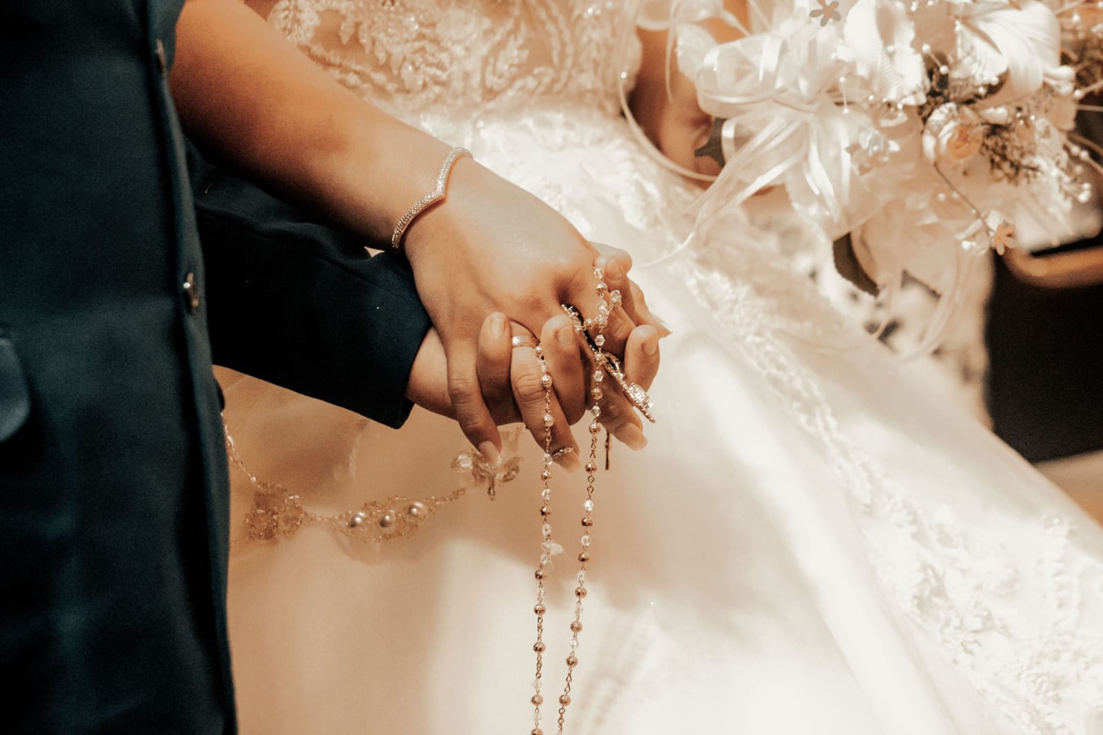 Close-up of a bride and groom holding hands with a rosary at their wedding. (Representative Cover Image Source: Pexels | Photo by Paul Otero Garcia)