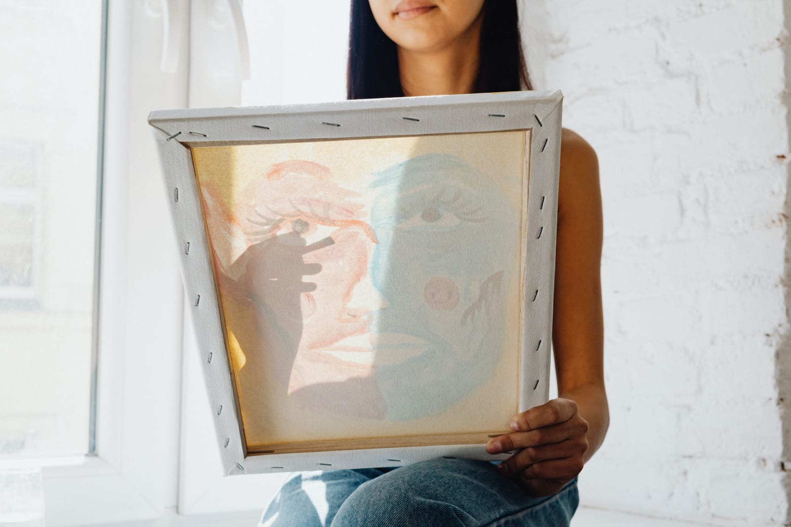 A woman holding and viewing a canvas painting in a bright, sunlit room, showcasing shadows. (Representative Cover Image Source: Pexels | Photo by https://kaboompics.com/)
