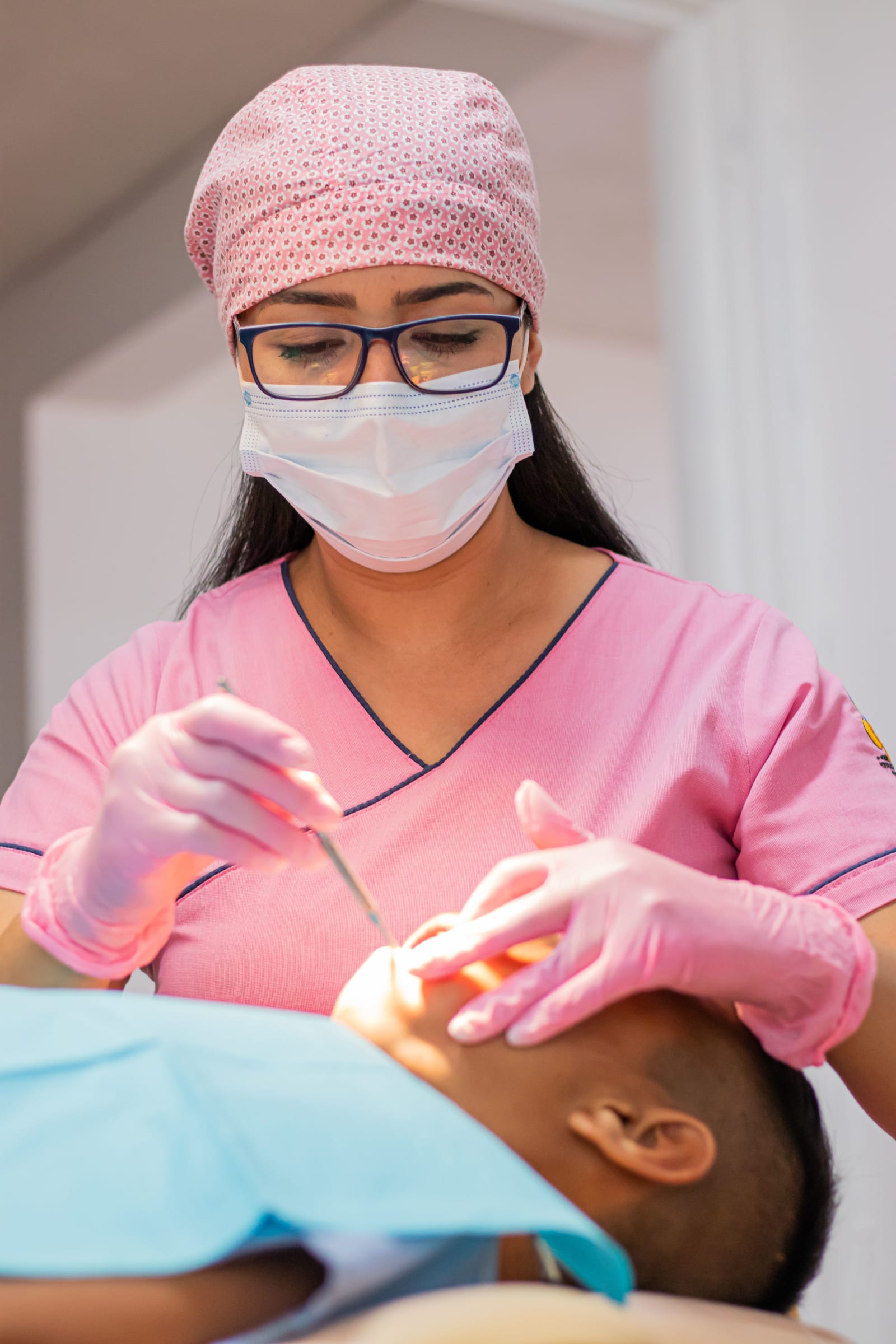 Dentist in pink scrub treating a patient.
