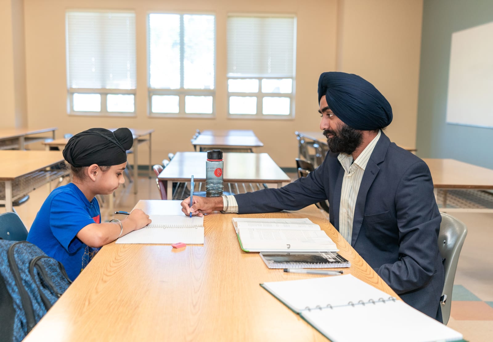 A male teacher helping a young student with studies in a classroom environment. (Representative Cover Image Source: Pexels | Photo by World Sikh Organization of Canada)