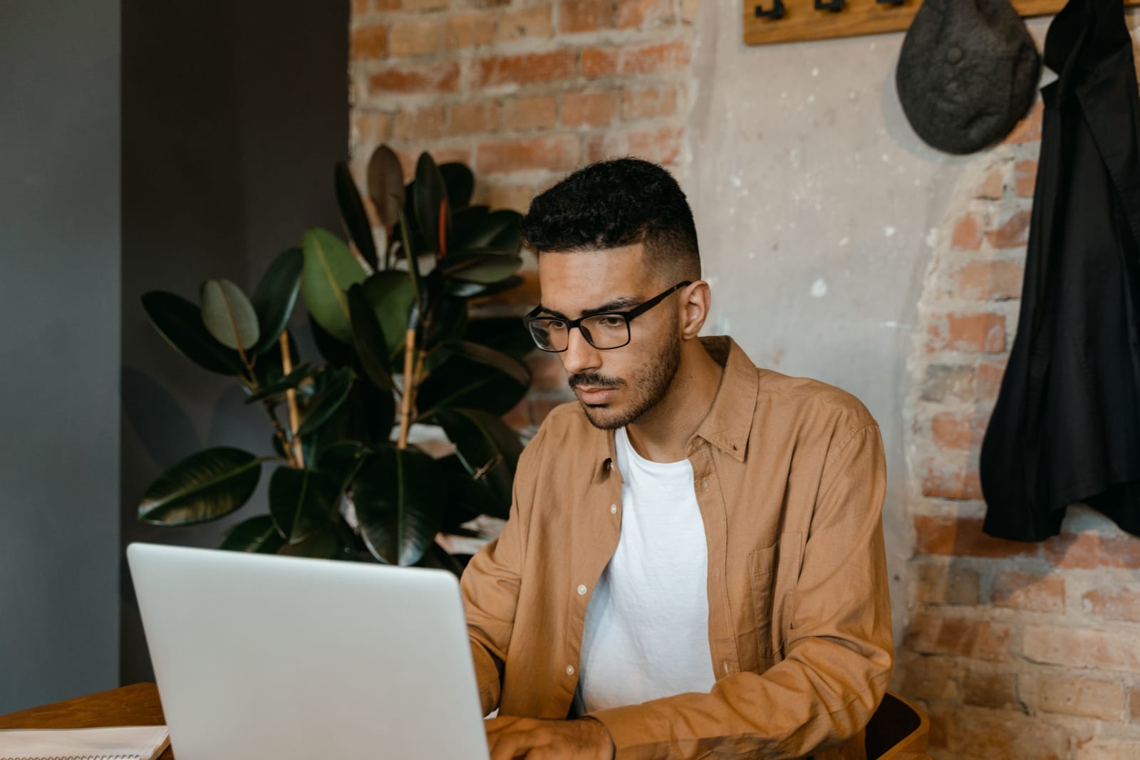 A man in glasses working on a laptop in a cozy cafe with brick walls and plants. (Representative Cover Image Source: Pexels | Photo by Mart Production)