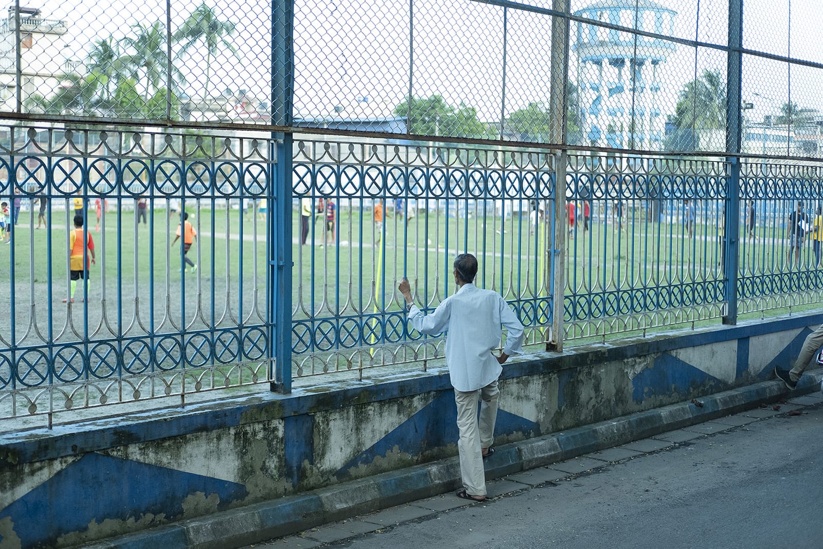Man watches from outside a grilled playground as kids play inside.