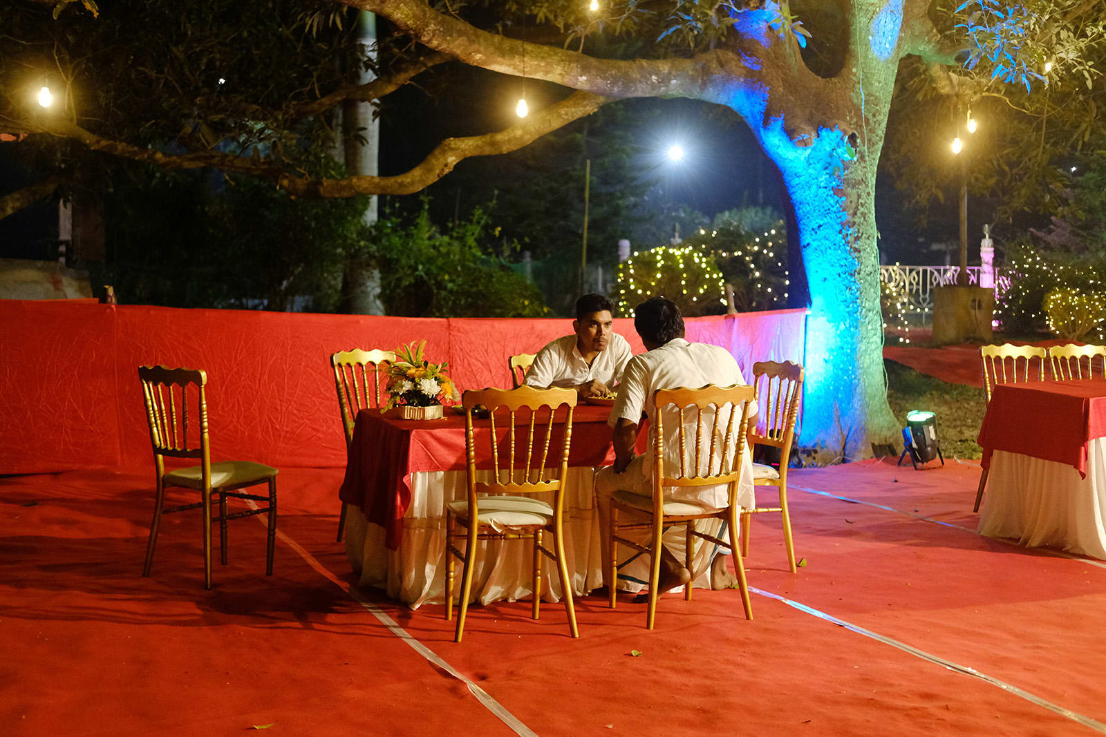 Two guests chat while eating at a wedding feast, in an empty location.