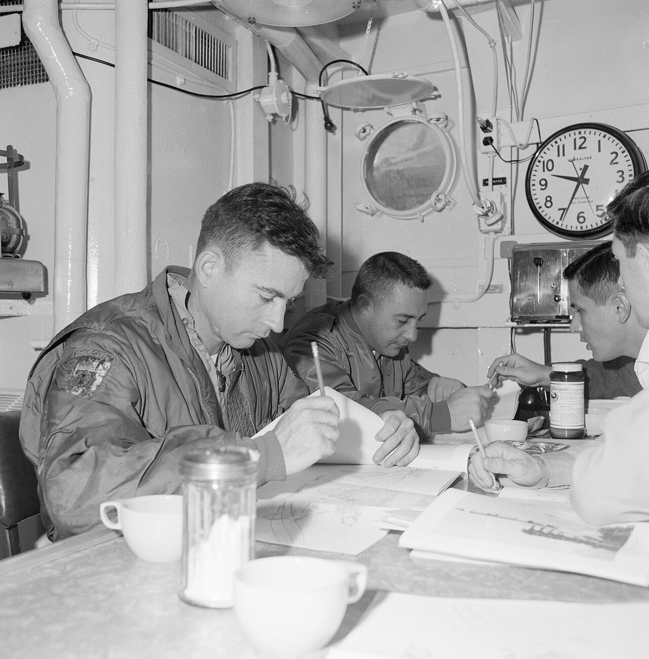Astronauts John W. Young and Virgil I. Grissom receive instructions for getting out of the Gemini spacecraft after a water landing during a briefing in the galley of the NASA Motor Vessel Retriever enroute to the training site 15 miles south of Galveston, in the Gulf of Mexico.