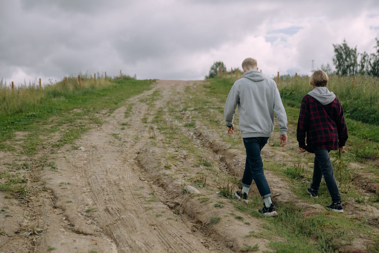 Two individuals walking on a rural dirt path surrounded by grass under a cloudy sky. (Representative Image Source: Pexels | Photo by cottonbro studio)