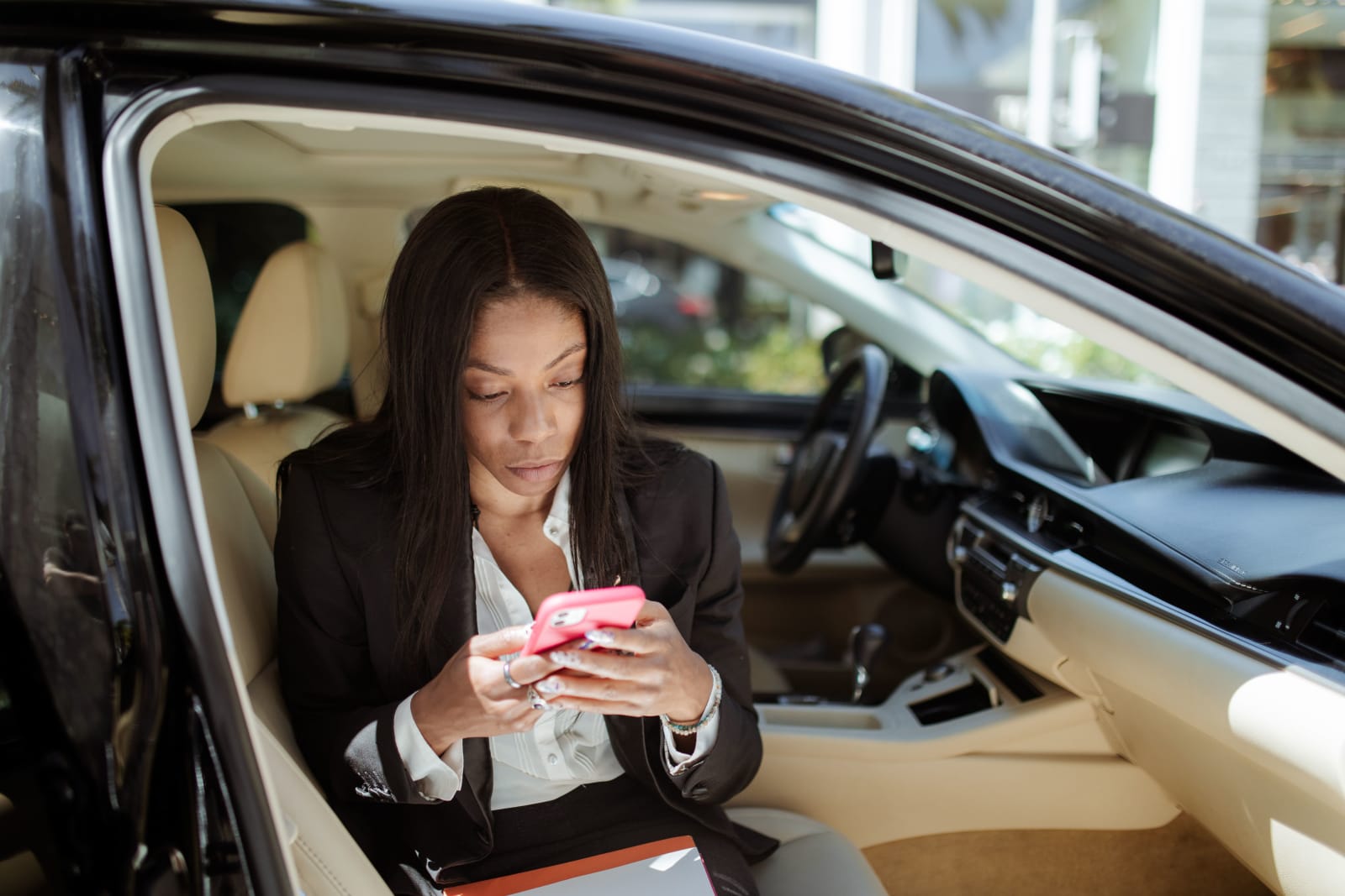 A businesswoman uses her smartphone while seated in a car, focusing intently on the screen. (Representative Image Source: Pexels | Photo by RDNE Stock Project)